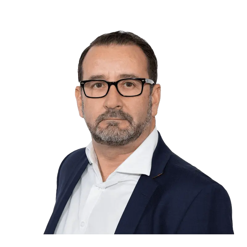 Ein Mann mit kurzen dunklen Haaren, Brille und Bart trägt einen marineblauen Blazer und ein weißes Hemd. Vor einem schlichten Hintergrund blickt er direkt in die Kamera.