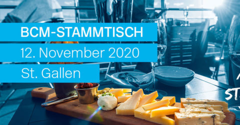 A table set with a platter of assorted cheeses and a glass of wine, illuminated by warm sunlight. The text overlay reads "BCM-Stammtisch St. Gallen, 12. November 2020," creating an inviting and cozy atmosphere.
