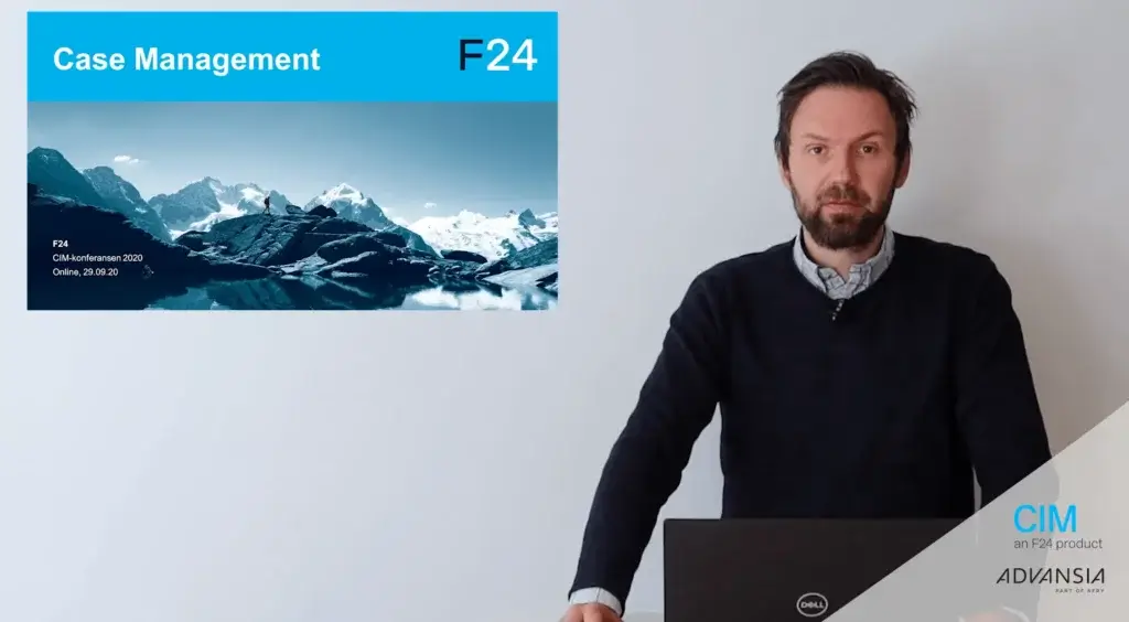 A man with a beard is standing behind a laptop, speaking in front of a presentation slide titled "Case Management F24." The slide features a landscape of snow-capped mountains and a lake. Logos for CIM and ADVANSIA appear at the bottom right.