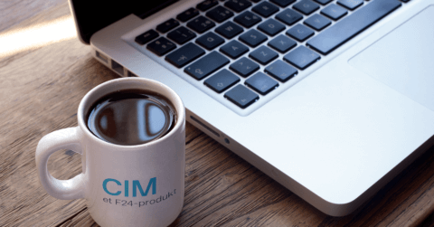 En kaffekopp med CIM-logo, bærbar pc