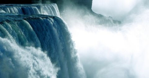 Close-up of a waterfall with cascades of water flowing over the edge. Mist rises from the waterfall, creating a dreamy, picturesque scene. The image captures the power and beauty of the natural landscape.