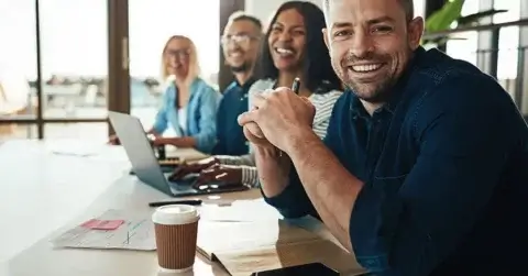 Smiling businessman sitting with a diverse group of coworkers during a meeting together at a table in an office