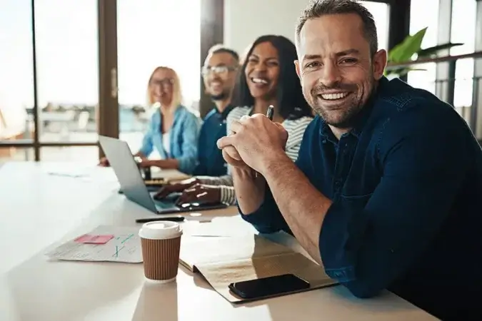 Smiling businessman sitting with a diverse group of coworkers during a meeting together at a table in an office