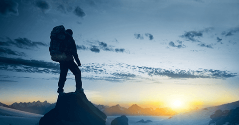 Mann med sekk på toppen av et fjell. Solnedgang.