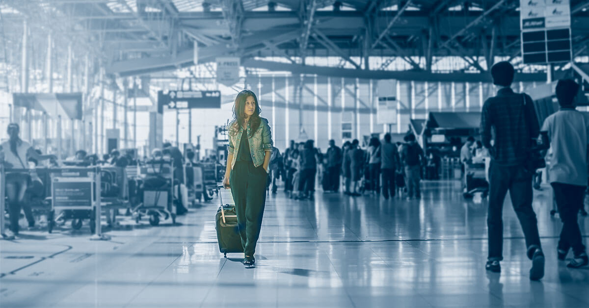 En kvinne i dress går selvsikkert gjennom den travle flyplassterminalen, med kofferten på slep. Omgitt av mennesker, store vinduer og overliggende skilt funderer hun: "Vet du hvor dine medarbeidere er akkurat nå?" mens hun navigerer i den pulserende scenen.