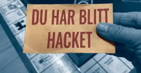 En hånd holder et kort med "DU HAR BLITT HACKET" over et brettspill, satt mot en litt uskarp, blåtonet bakgrunn. Dette øyeblikksbildet fremhever viktigheten av sjekklister ved cyberangrep mens du navigerer i både digitale og analoge verdener.