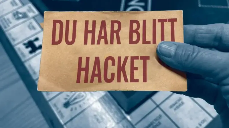 En hånd holder et kort med "DU HAR BLITT HACKET" over et brettspill, satt mot en litt uskarp, blåtonet bakgrunn. Dette øyeblikksbildet fremhever viktigheten av sjekklister ved cyberangrep mens du navigerer i både digitale og analoge verdener.