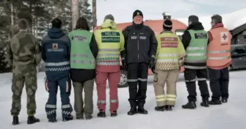Politi i fokus. Ved siden av med ryggen til står røde kors, brannvesen, ambulansearbeider