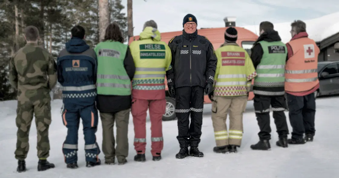 Politi i fokus. Ved siden av med ryggen til står røde kors, brannvesen, ambulansearbeider