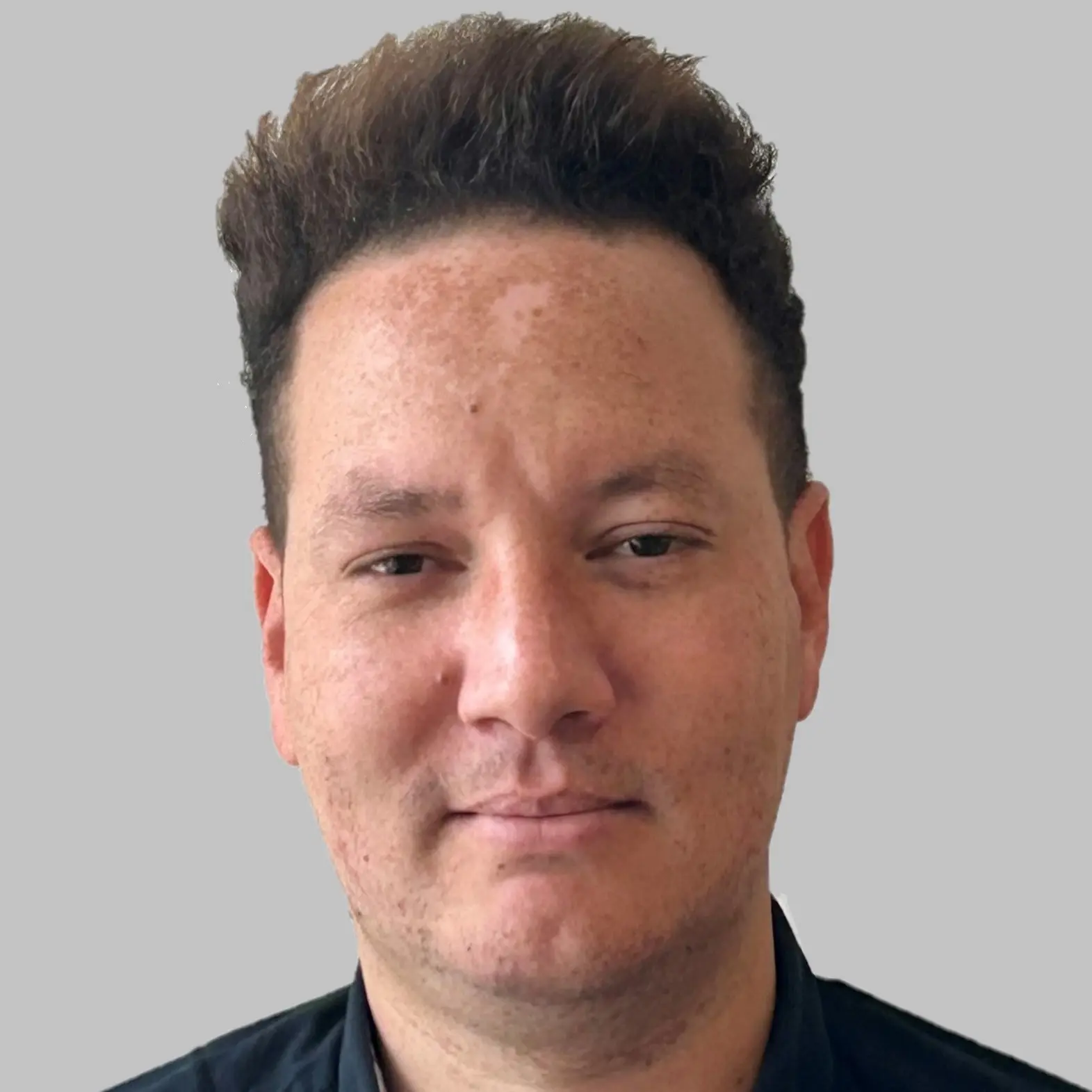 A person with short, curly brown hair and light skin is facing the camera with a neutral expression, wearing a dark shirt against a plain light gray background at a resilience conference in London.