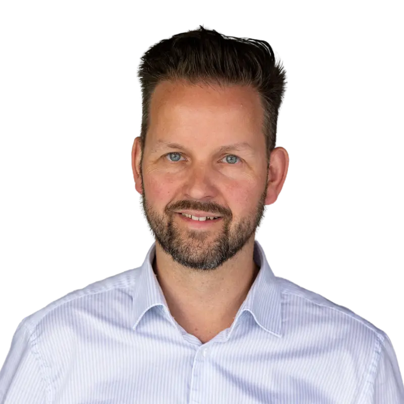 Ein Mann mit kurzen braunen Haaren, einem Bart und blauen Augen lächelt. Er trägt ein hellblaues Button-up-Hemd mit dünnen Streifen und stellt eine der F24-Tochtergesellschaften dar, die vor einem schlichten weißen Hintergrund fotografiert wurde.