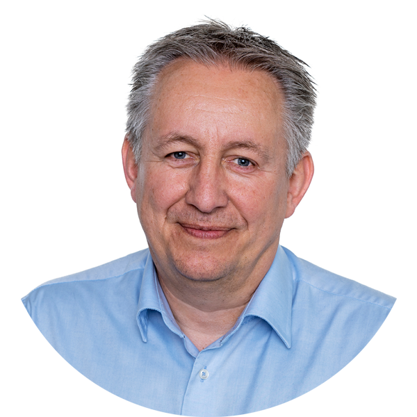 A middle-aged man with short gray hair, wearing a light blue button-up shirt, smiles gently against a plain white background.