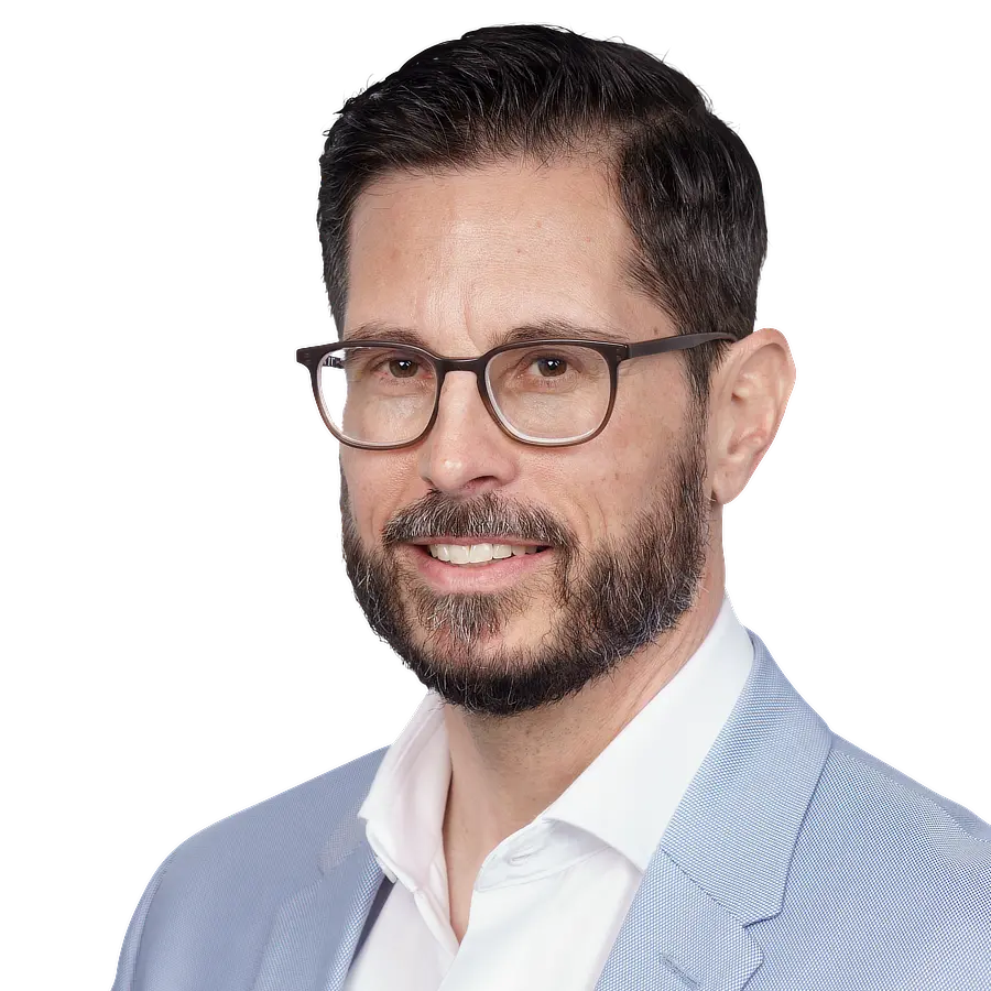 A man with short dark hair, a beard, and glasses is smiling in a professional portrait for the F24 Experience Tour München – Event für Resilienz & Krisenmanagement, wearing a light blue blazer over a white shirt and facing slightly to the left.