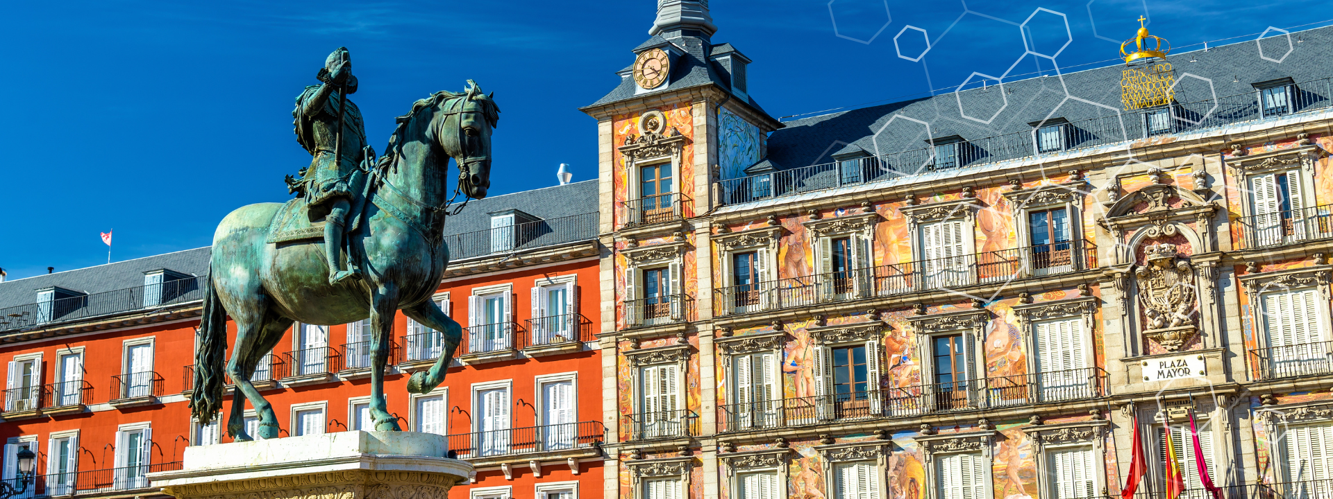 A bronze equestrian statue stands in the center of Plaza Mayor in Madrid, Spain, surrounded by colorful, historic buildings with numerous windows and shutters under a clear blue sky.
