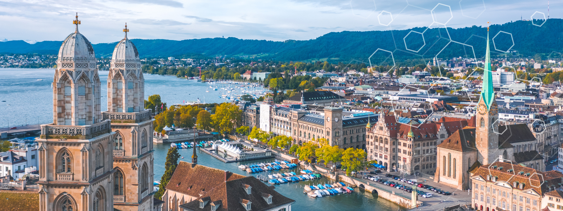 Vue aérienne de Zurich avec les tours jumelles de l'église Grossmünster, la rivière Limmat avec des bateaux, des bâtiments historiques et des collines verdoyantes sous un ciel bleu.