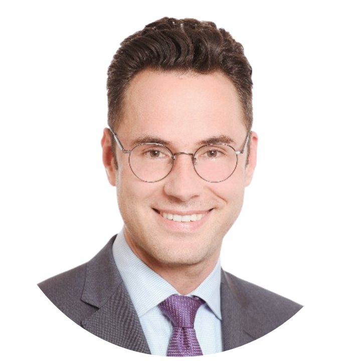 A man with short, dark hair wearing round glasses, a grey suit, a light blue shirt, and a purple tie smiles at the camera. The background is white—highlighting confidence like eine starke Schnittstelle für den Ernstfall: FACT24 ENS+ in Winguard.