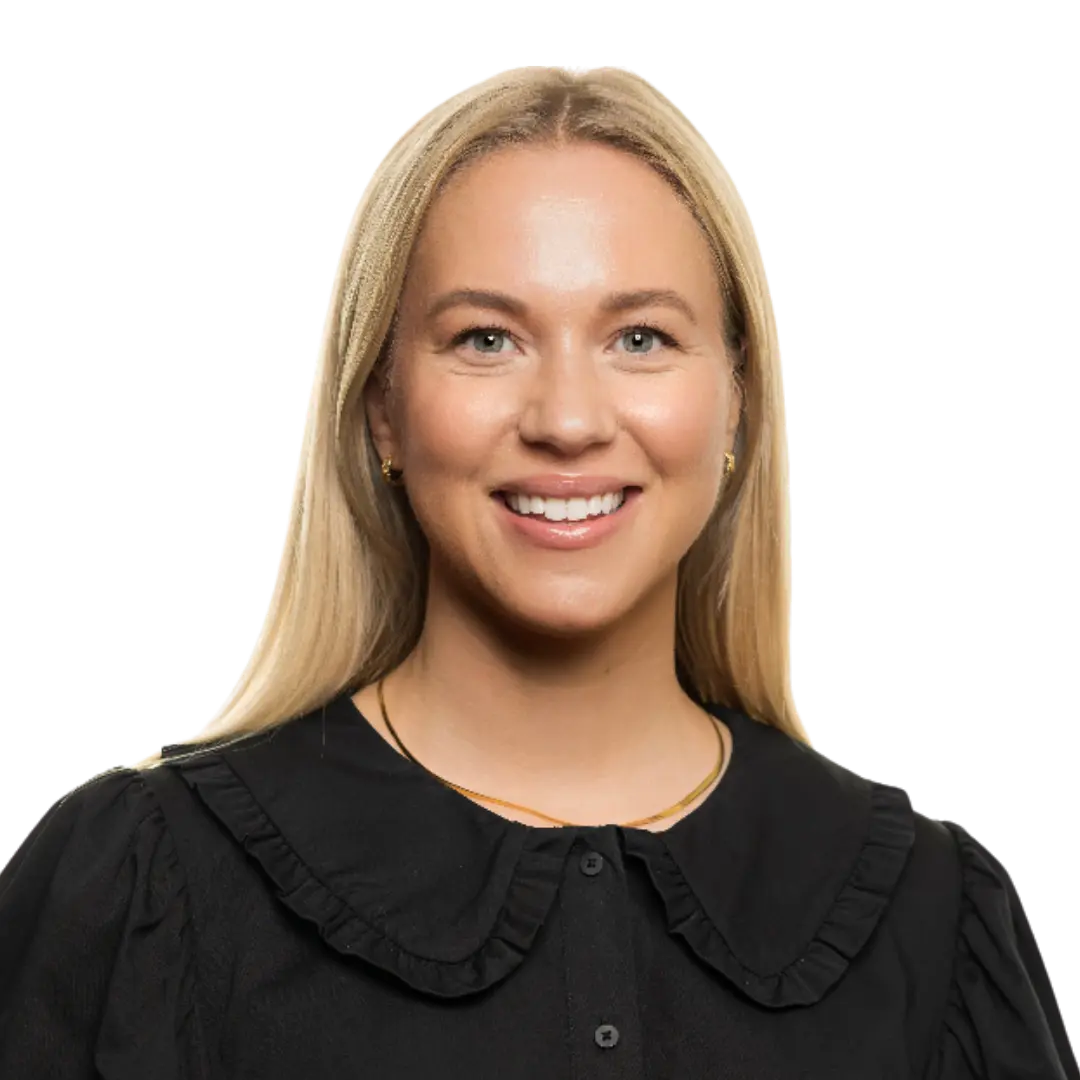 A woman with straight blonde hair, wearing a black blouse with a ruffled collar and a gold necklace, smiles at the camera against a plain white background, capturing the effortless elegance often seen in Norway.