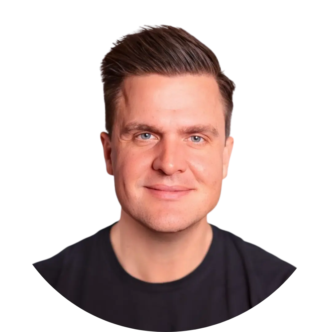 A man from Germany with short brown hair styled upward, light skin, and blue eyes, smiling slightly. He is wearing a black shirt and is pictured against a plain white background.