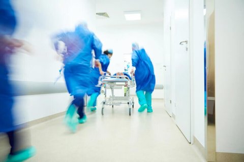 
Medicinsk personal i blå kläder rusar fram med en patient på bår genom en sjukhuskorridor.