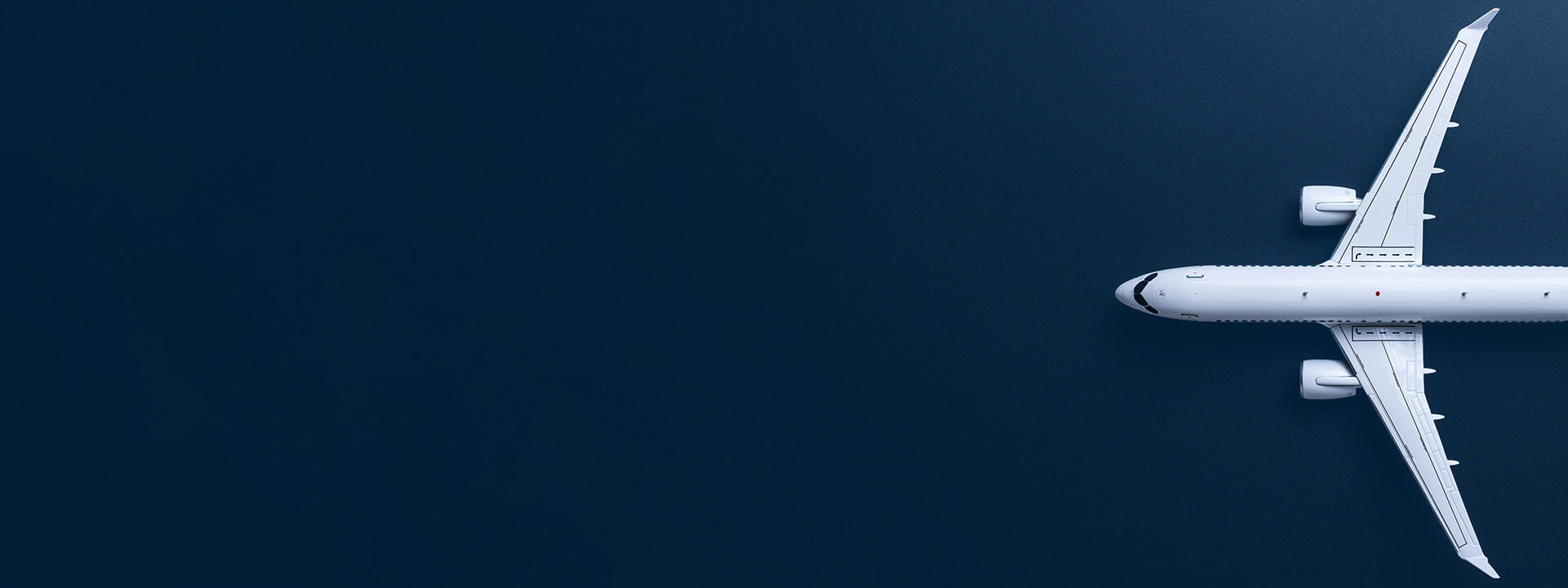A white airplane is flying over a dark blue background, captured from above with the plane positioned on the right side and empty space on the left.