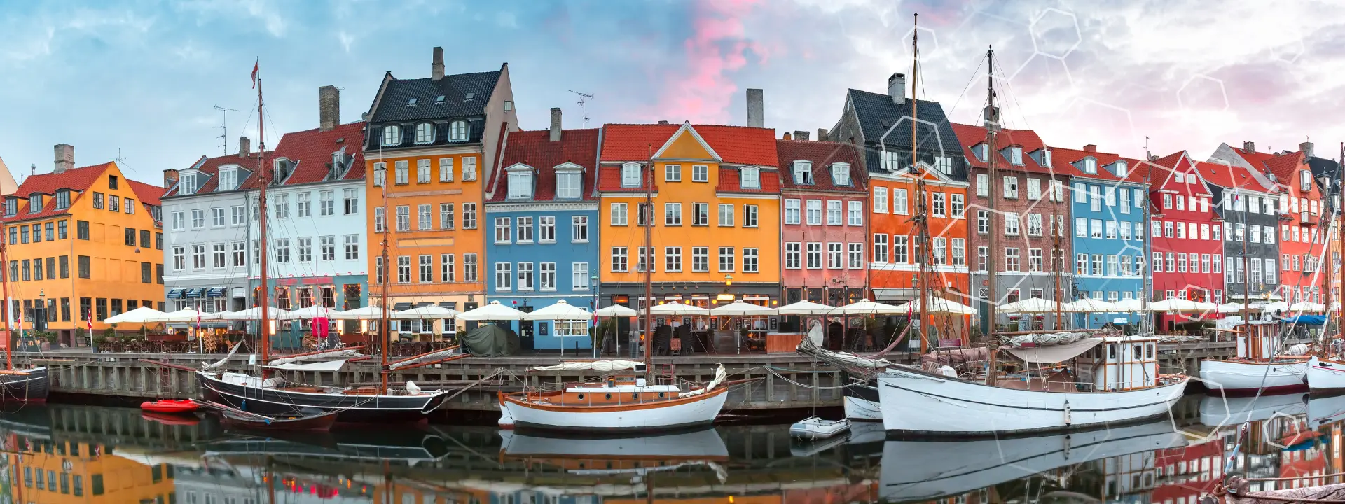 Las coloridas casas adosadas se alinean a lo largo de la orilla de Nyhavn, en Copenhague (Dinamarca), con barcos atracados a lo largo del canal y mesas al aire libre bajo las sombrillas de las cafeterías a pie de calle.