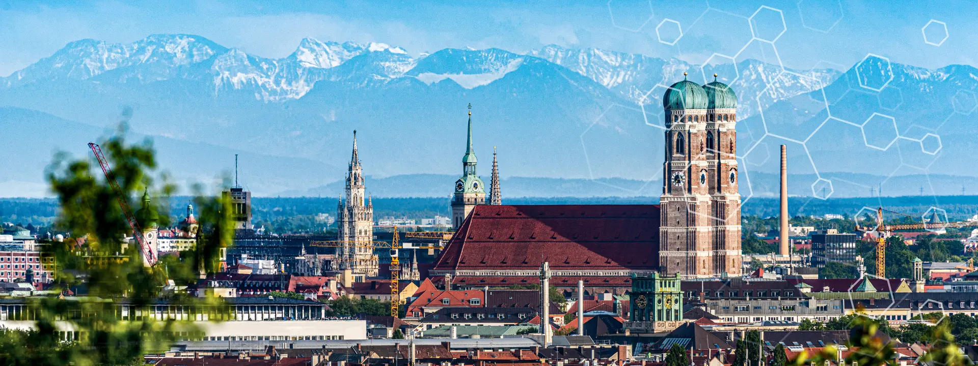 Et bybilde av München med historiske bygninger og kirketårn i forgrunnen, og snødekte Alper i bakgrunnen under en blå himmel. Diskrete geometriske mønstre ligger over himmelen.
