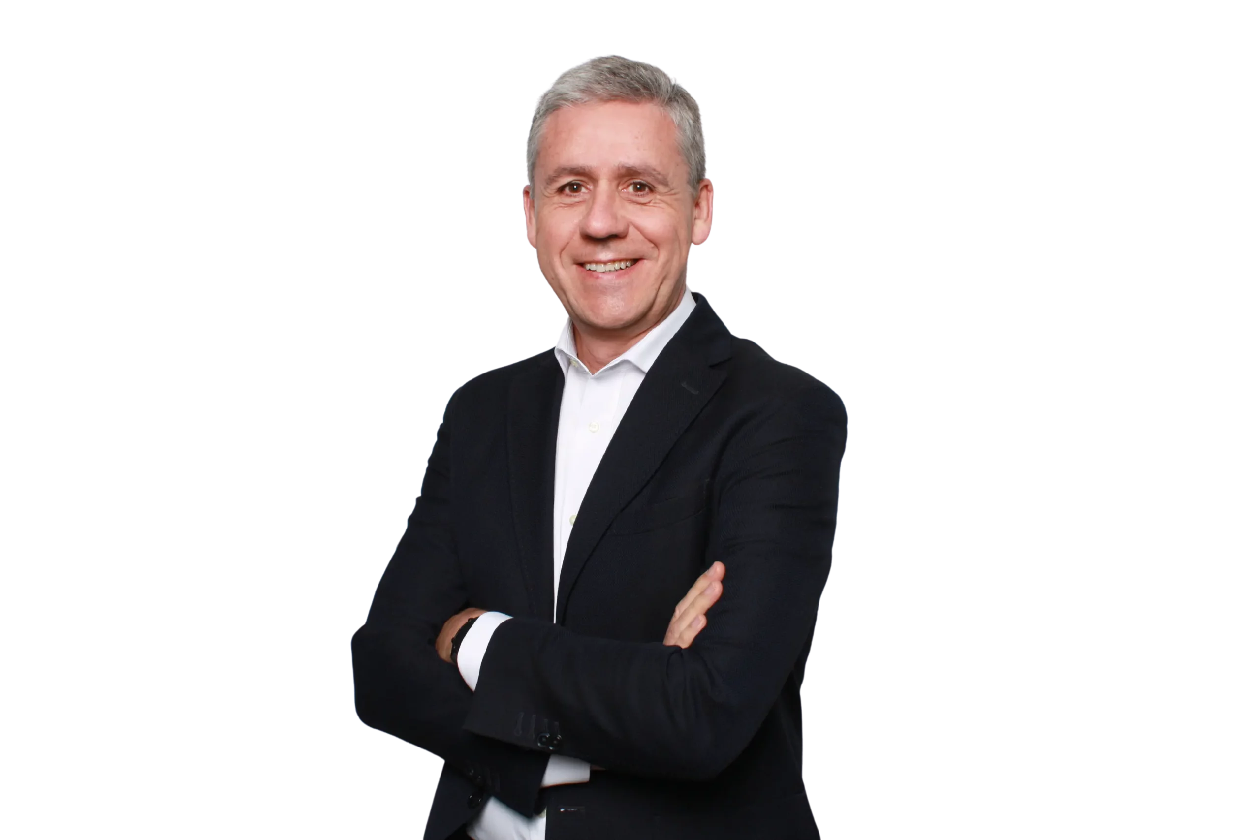Un hombre de mediana edad, con el pelo corto y canoso, sonríe de pie, con los brazos cruzados, vestido con una chaqueta de traje oscura y una camisa blanca, frente a un fondo blanco liso.