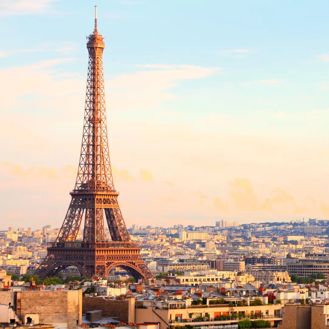 The Eiffel Tower stands tall against a pastel sky at sunset, surrounded by city buildings and rooftops in Paris, France—an iconic view you’ll cherish. For details or inquiries, contact f24.