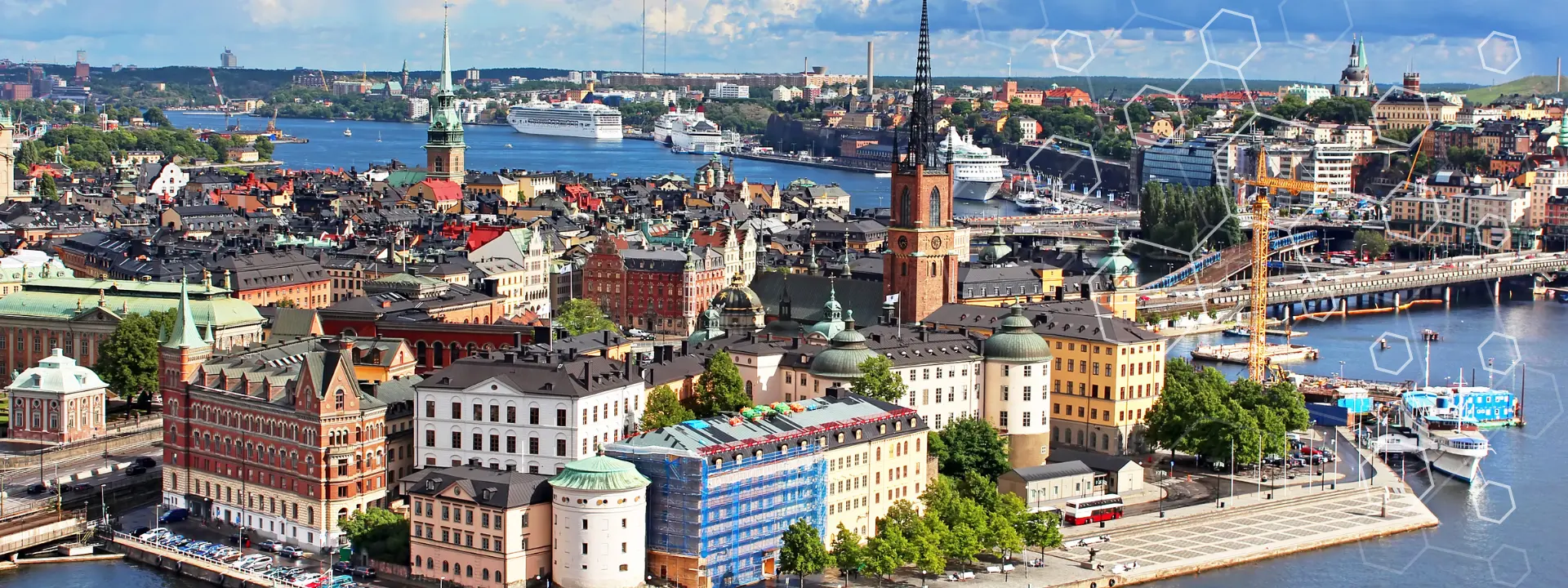 Ein Panoramablick auf Stockholm mit farbenfrohen historischen Gebäuden, Kirchtürmen und Wasserwegen, an deren Ufern Boote vor Anker liegen und im Hintergrund ein Kreuzfahrtschiff zu sehen ist.