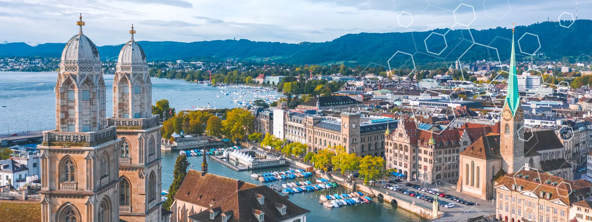 Luftfoto av Zürich i Sveits, med historiske bygninger, kirketårn, en elv med båter og fjell i bakgrunnen under en klar himmel, med digital sekskantgrafikk lagt over bildet.