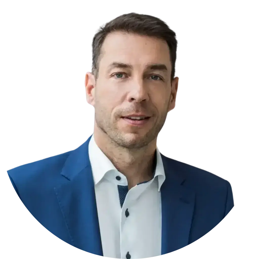 A man wearing a blue suit jacket and white dress shirt is facing the camera and smiling slightly, embodying the confidence of someone who understands how operational resilience works. The background is plain white.