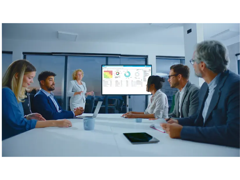 Eine Frau präsentiert während einer Schulung zum Krisenmanagement ihren Kollegen, die um einen Konferenztisch sitzen, ein Daten-Dashboard auf einem Bildschirm.